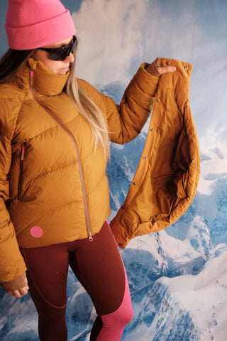 SENIQ model Tina wears Powder Puff Down Jacket in Hotty Toddy with Cabin Fever Merino Wool Leggings for insulated warm weather gear that's cozy and vibrant for ski snowboard outerwear
