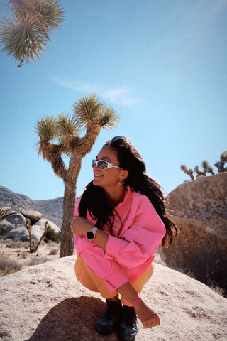 Woman in Joshua Tree wearing outdoor technical apparel by SENIQ. Dirtpop Trek Jacket and Tectonic Pant. Bright vibrant colors, optimal performance.