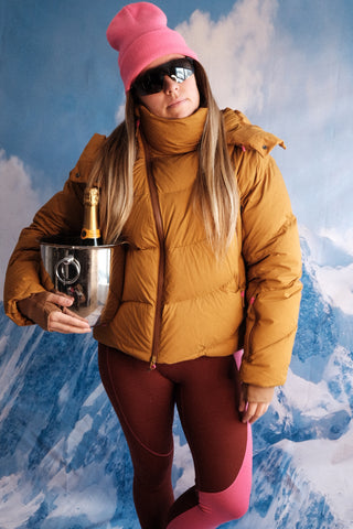 SENIQ model Tina wears Powder Puff Down Jacket in Hotty Toddy with Cabin Fever Merino Wool Leggings for insulated warm weather gear that's cozy and vibrant for ski snowboard outerwear