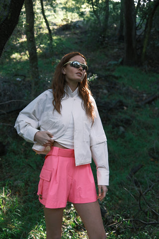 Woman in the woods wearing SENIQ Trailmix Short, Dirtpop Trek Jacket, Oasis Tank