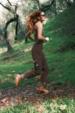 Woman running through woods wearing SENIQ Technical Outdoor clothing. Trailmix pants with Oasis Tank