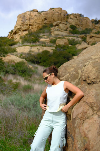 Woman leaning against a boulder wearing SENIQ Field Crop Tank