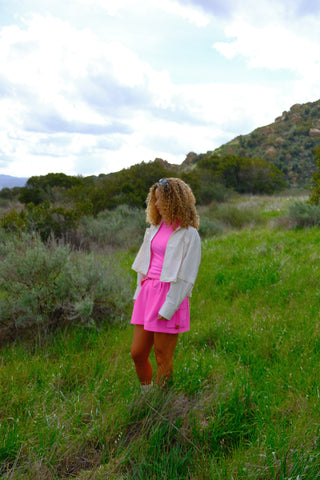 Woman standing in grassy patch wearing SENIQ Trailmix Short, Oasis Tank, and Dirtpop Trek Jacket