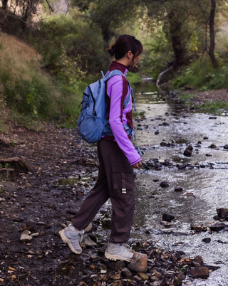 Woman wearing a SENIQ Joytrek Midlayer Fleece in Brambleberry standing on a mountain with a clear blue sky.